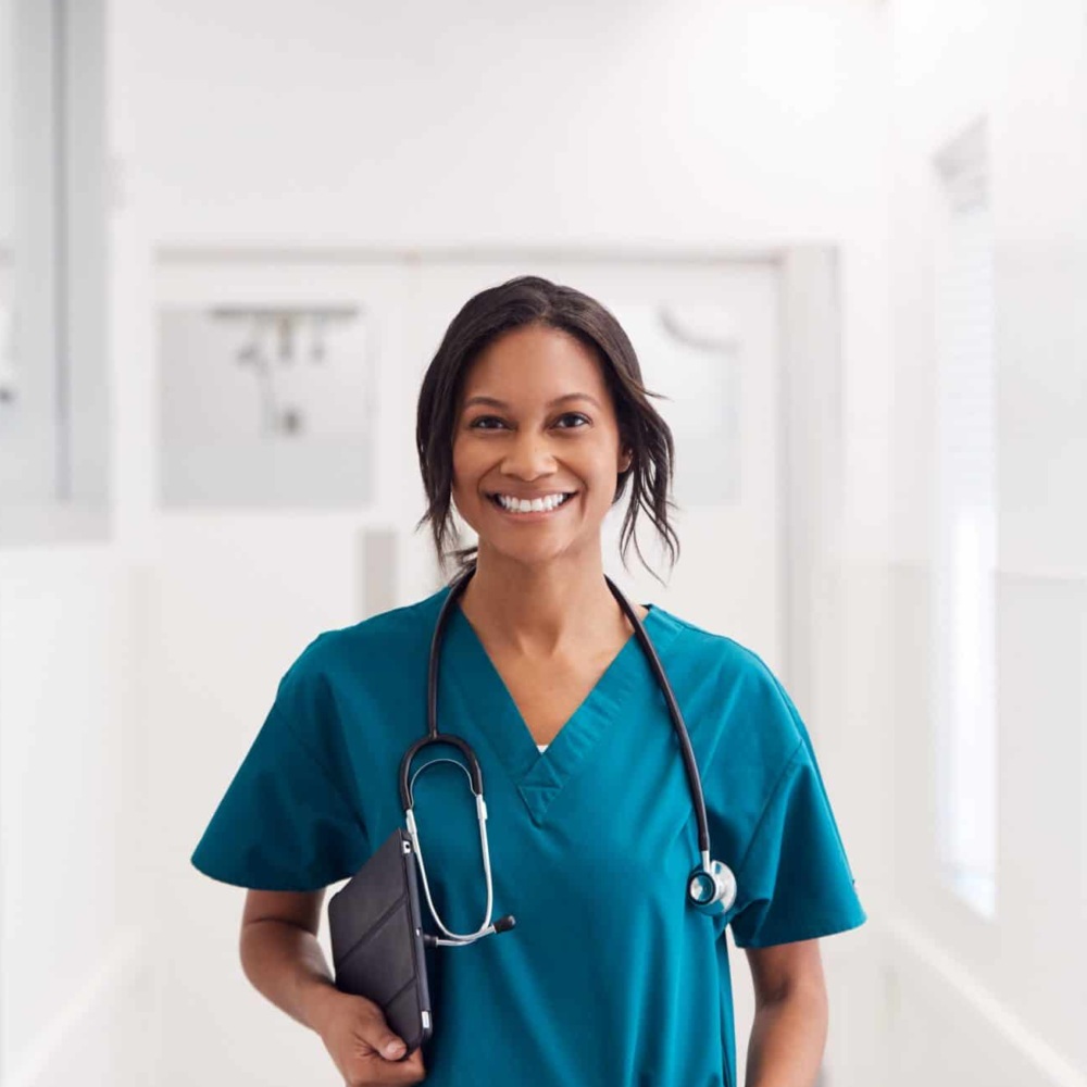 Portrait Of smiling female doctor wearing scrubs In hospital corridor holding digital tablet.
